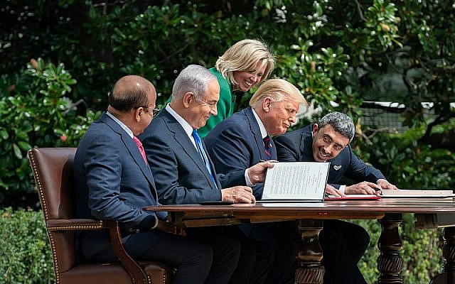 Then-US chief of protocol Cam Henderson assists then-US president Donald J. Trump, Minister of Foreign Affairs of Bahrain Dr. Abdullatif bin Rashid Al-Zayani, then-prime minister Benjamin Netanyahu, and Minister of Foreign Affairs for the United Arab Emirates Abdullah bin Zayed Al Nahyan with the documents during the signing of the Abraham Accords, September 15, 2020, on the South Lawn of the White House. (Official White House Photo Andrea Hanks, via Wikimedia Commons)