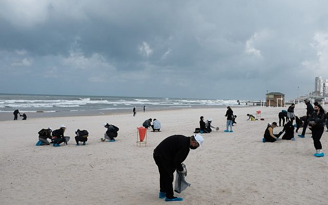 People clean tar off the Bat Yam beach following an offshore oil spill which drenched most of the Israeli coastline, March 2, 2021. (Tomer Neuberg/Flash90)
