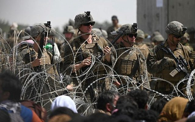US soldiers stand guard behind barbed wire as Afghans sit on a roadside near the military part of the airport in Kabul on August 20, 2021, hoping to flee from the country after the Taliban's military takeover of Afghanistan. (Photo by Wakil KOHSAR / AFP)