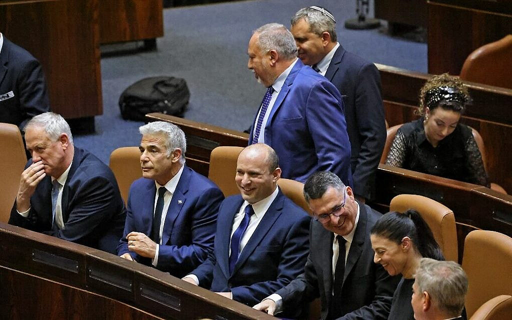 Sitting from left to right: Defense Minister Benny Gantz, Foreign Minister Yair Lapid, Prime Minister Naftali Bennett, Justice Minister Gideon Sa'ar, Transportation Minister Merav Michaeli and Health Minister Nitzan Horowitz, as Finance Minister Avigdor Lieberman and Housing Minister Ze'ev Elkin walk past after a special Knesset plenum session to approve the new government, June 13, 2021. (Emmanuel Dunand/AFP)