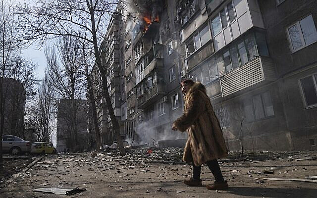 A woman walks past a burning apartment building after shelling in Mariupol, Ukraine, Sunday, March 13, 2022. (AP Photo/Evgeniy Maloletka)