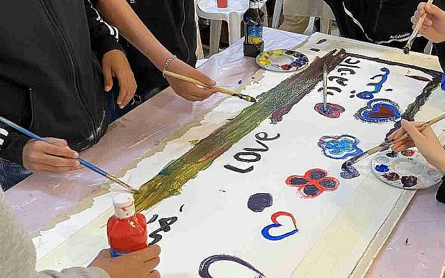 Students paint the word "Love" in Arabic, Hebrew, and English on banners at the Mishkan Museum of Art as part of a shared learning project organized by The Abraham Initiatives. Photo by the author.