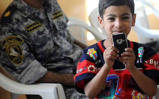 A local Iraqi boy takes photographs with a cell phone during an opening ceremony for a new vocational school facility in the Shawra Wa Um Jidir area of eastern Baghdad, Iraq on June 11, 2022. (DVIDSHUB, via Wikimedia Commons)