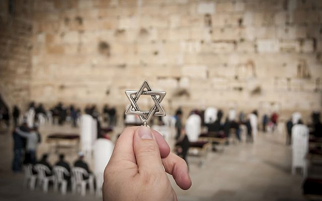 JERUSALEM, ISRAEL. February 15, 2019. Hand holding a Star of David, a Jewish national and religious symbol in front of the Western wall of the Jewish Temple in the Old city of Jerusalem. Tisha B'Av