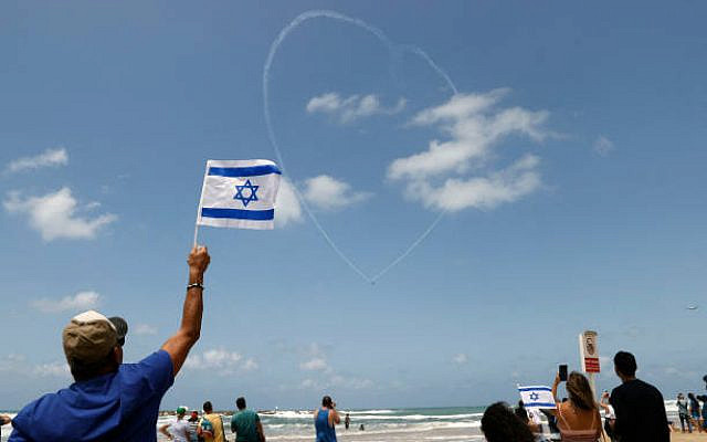 An Israeli man waves a flag as Israeli Efroni T-6 Texan II planes perform stunts in the sky above the Mediterranean coastal city of Tel Aviv on May 5, 2022, as Israel marks Independence Day (Yom HaAtzmaut), 74 years since the establishment of the Jewish state. - Israel's first prime minister David Ben-Gurion declared the existence of the State of Israel in Tel Aviv in 1948, ending the British mandate. (Photo by JACK GUEZ / AFP) (Photo by JACK GUEZ/AFP via Getty Images)