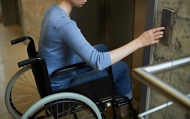 Illustrative. A woman seated in a wheelchair pushes the button to call an elevator. (iStock)