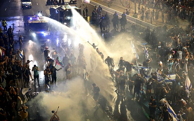 Demonstrators are sprayed with water cannons by riot police during a protest against the government's judicial reform plan in Tel Aviv on July 24, 2023. (JACK GUEZ / AFP)