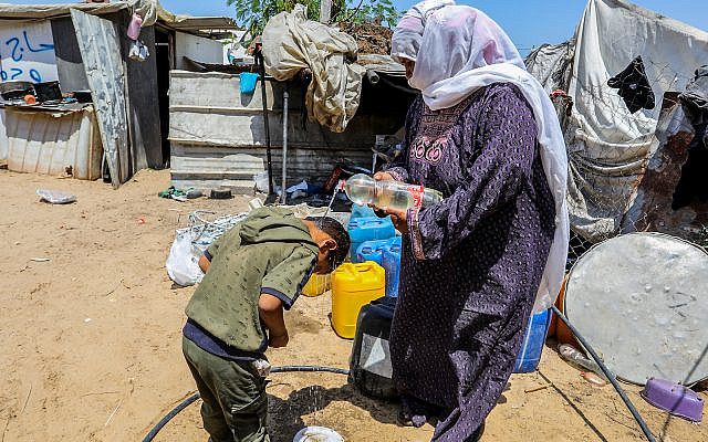 A Palestinian woman pours water on a child outside her tent, during a hot summer day in Rafah in the southern Gaza Strip on July 31, 2023. (Abed Rahim Khatib/Flash90)