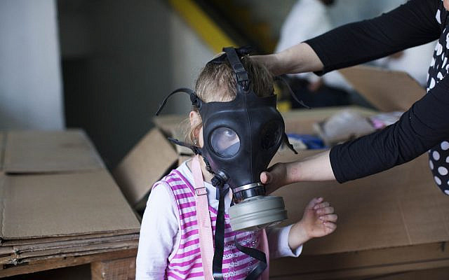 Illustrative: A woman shows her child how to put on a gas mask at a gas mask distribution center in Jerusalem, August 27, 2013. (Yonatan Sindel/Flash90)