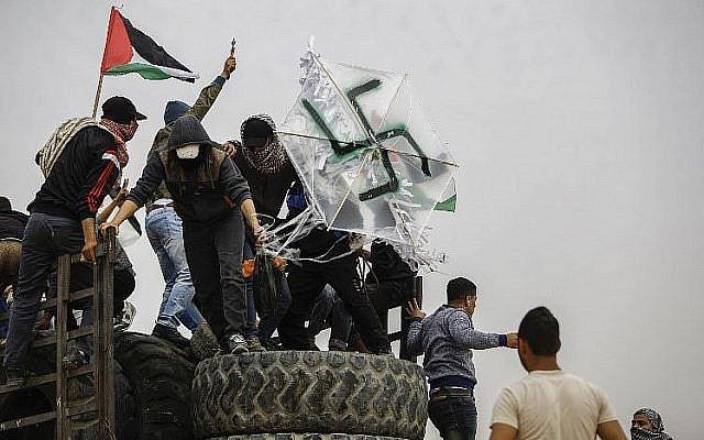 Palestinians hold a kite adorned with a swastika that is carrying a bomb near the border with Israel east of Gaza City, on April 20, 2018. (AFP Photo/Mohammed Abed)