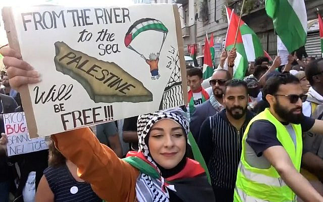 An anti-Israel protestor holds a sign depicting a Hamas paraglider and the slogan "From the River to the Sea", which calls for the death of all Israelis.