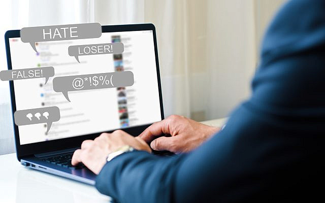 Image: Shutterstock/SergeiShimonovichm -Hate Speech concept. a man works at a laptop and receives messages with notification icons of bullying on social networks and hatred on the Internet