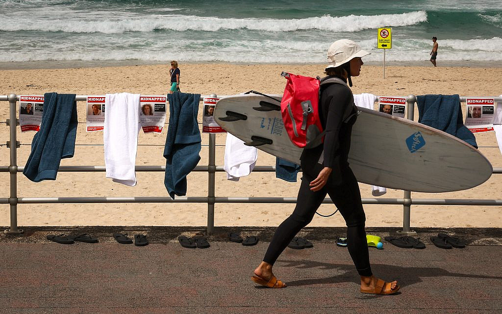 A surfer carrying her board walks past posters, towels and flip-flops that are part of a protest organized by the Australian Jewish community at Bondi Beach in Sydney on November 2, 2023 to highlight the plight of hostages held by Hamas (David Gray / AFP)