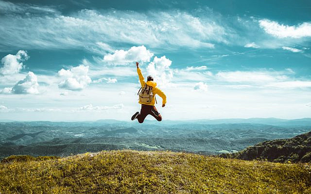 Happy man with open arms jumping on the top of mountain - Hiker with backpack celebrating success outdoor - People, success and sport concept