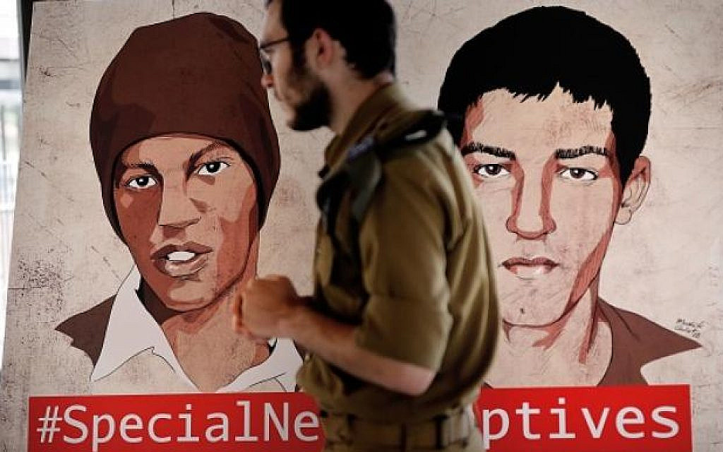 A soldier walks past a painted poster of Hisham Al-Sayed (R) and Avera Mengistu (L), two Israelis held by Hamas since 2014, when they crossed into Gaza, during a press conference organized by the captives' families calling for their release, in Jerusalem, on September 6, 2018. (THOMAS COEX / AFP)