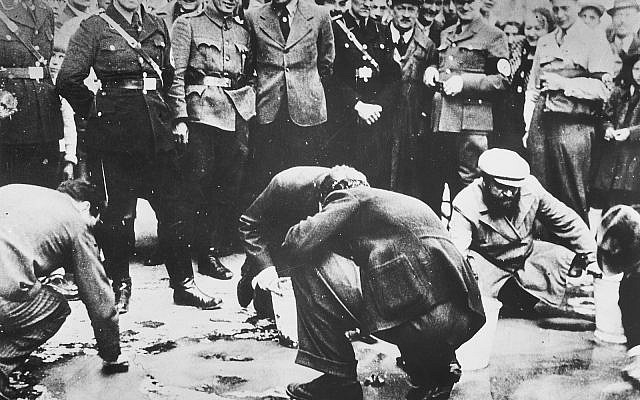 Austrian Nazis and local residents look on as Jews are forced to get on their hands and knees and scrub the pavement. Vienna, Austria, 1938 (PD via Wikimedia)