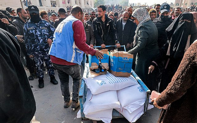 Workers of the United Nations Relief and Works Agency for Palestine Refugees (UNRWA) hand out flour rations and other supplies to people at an UNRWA warehouse in Rafah in the southern Gaza Strip on December 12, 2023. (Mohammed Abed/AFP)