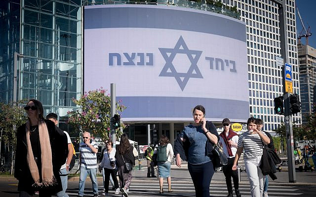 People walk by a large billboard reading "Together we will win" at Azrieli, in Tel Aviv. December 19, 2023. (Miriam Alster/Flash90)