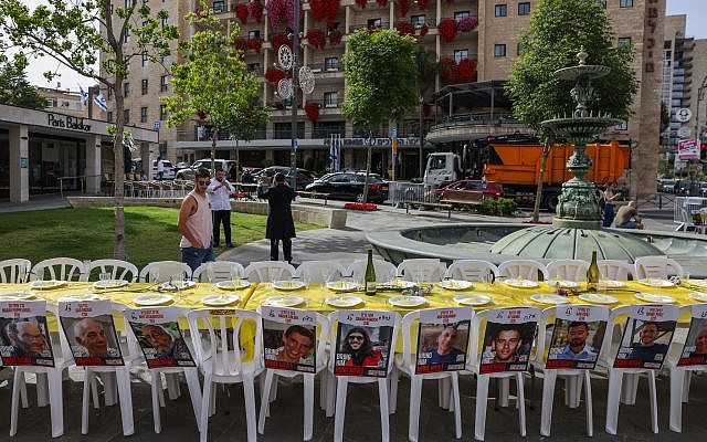 People walk next to a seder table with pictures of the hostages held in the Gaza Strip by the terror group Hamas, in Jerusalem, April 22, 2024. (Chaim Goldberg/ Flash90)