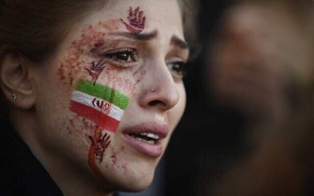 تصویر: یکی از معترضان با پرچم ایران و دست های قرمزی که روی صورت خود رنگامیزی کرده در راهپیمایی حمایت از تظاهرات ایرانیان در پاریس، ۹ اکتبر ۲۰۲۲ که در پی جان باختن مهسا امینی، زن ایرانی در ایران برگزار شد شرکت کرده است. (Julien de Rosa/AFP)