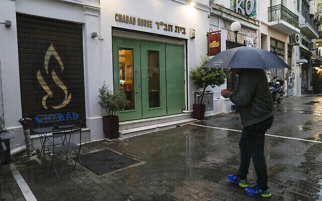 تصویر: مردی با چتر در ۲۸ مارس ۲۰۲۳ در مقابل مرکز یهودیان ایستاده که مقامات یونانی معتقدند از هدف-های حملهٔ برنامه-ریزی شده در مرکز آتن بوده است. (AP/Thanassis Stavrakis)