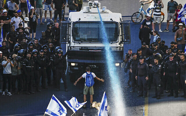 تصویر: در تظاهرات علیه طرح دولت نتانیاهو نخست وزیر برای اصلاح نظام قضایی، شخصی در اورشلیم در مقابل ماشین آبپاش پلیس اسرائيل که برای پراکندن تظاهرات-کنندگان بکار گرفته شد، ایستاده است؛ دوشنبه ۲۴ ژوئیه ۲۰۲۳، اورشلیم. (AP/Ariel Schalit)