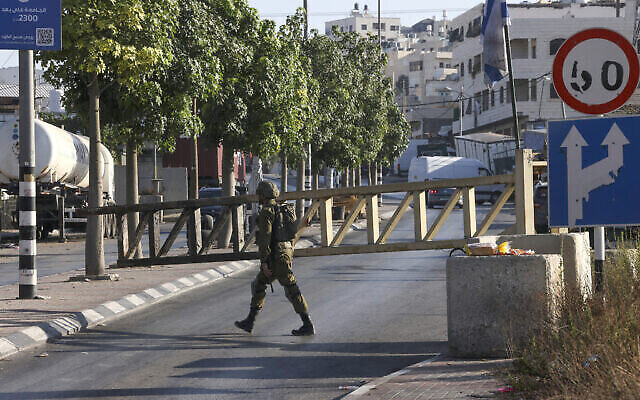 تصویر: سرباز اسرائیلی در ۲۲ اوت ۲۰۲۳، یک روز پس از تیراندازی تروریستی مرگبار ناحیه، حین نگهبانی در مقابل ورودی مسدود پاسگاهی در شهر حبرون، جنوب کرانهٔ باختری. (Hazem Bader/AFP)