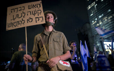 تصویر: یک کنشگر ضد-اصلاحات در تظاهرات در تل آویو با لباس سربازی، ۱۲ اوت ۲۰۲۳. روی پوستری که در دست دارد شعاری دربارهٔ شجاعت در میدان جنگ نوشته شده است. (Miriam Alster/Flash90)