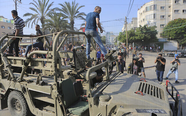 تصویر: فلسطینیان سوار بر خودرو نظامی که تروریست-های حماس از پایگاه ارتش اسرائیل در نزدیکی حصار نوار غزه که به تسخیر خود درآوردند برداشته-اند در شهر غزه می-گردند. (Abed Abu Reash/AP)