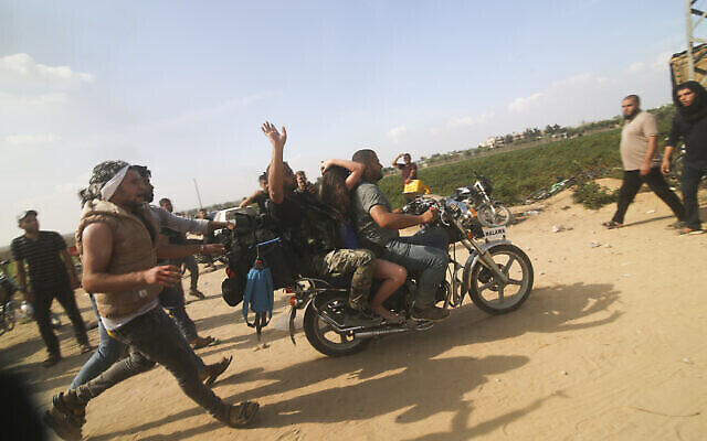 تصویر: فلسطینیان در روز ۷ اکتبر ۲۰۲۳ یک غیرنظامی اسرائیلی را (وسط) از کیبوتص کفار ازا ربوده و به نوار غزه می-برند. (Hatem Ali/AP)