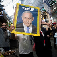 Un partisan du Likud tient une affiche de campagne montrant le Premier ministre  Benjamin Netanyahu sur le marché  Mahane Yehuda de Jérusalem, le 7 avril 2019 (Crédit : Yonatan Sindel/Flash90)