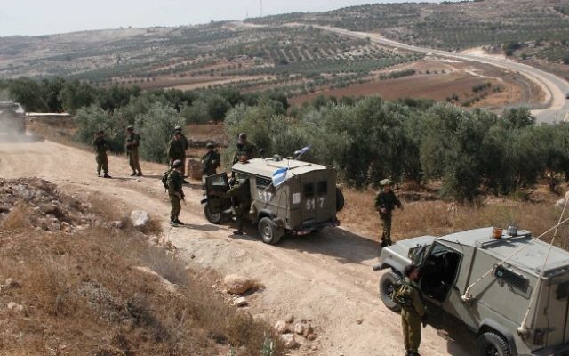 Des soldats israéliens protègent des Palestiniens lors d'une récolte d'olives à Hébron (Crédit : Najeh Hashlamoun/Flash90)