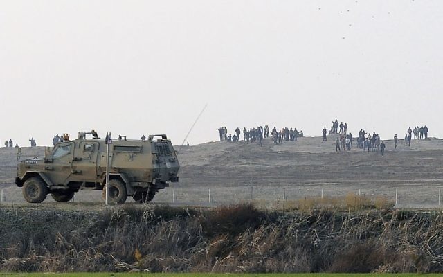 Des Palestiniens manifestent près de la barrière à la frontière entre Israël et la bande de Gaza alors qu'une jeep de l’armée israélienne patrouille à la frontière, 3 janvier 2014. (Crédit : David Buimovitch/Flash90)