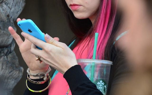 Jeune femme utilisant un smartphone de la marque Apple (Crédit : Frederic J. Brown)
