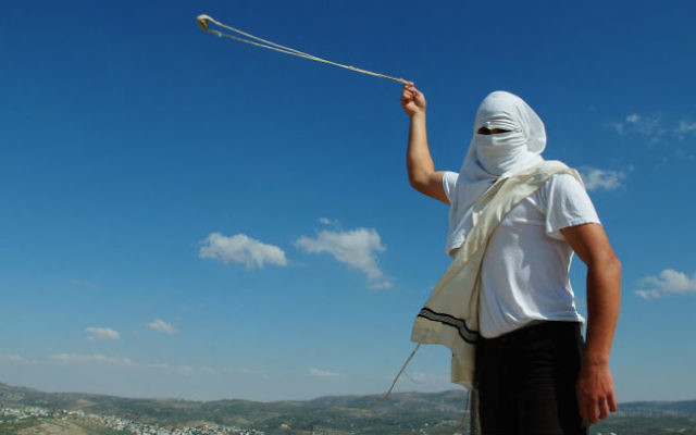 Un habitant masqué de Yitzhar, en Cisjordanie, lance des pierres avec une fronde, le 19 mai 2013. (Crédit : Mendy Hechtman/Flash90)