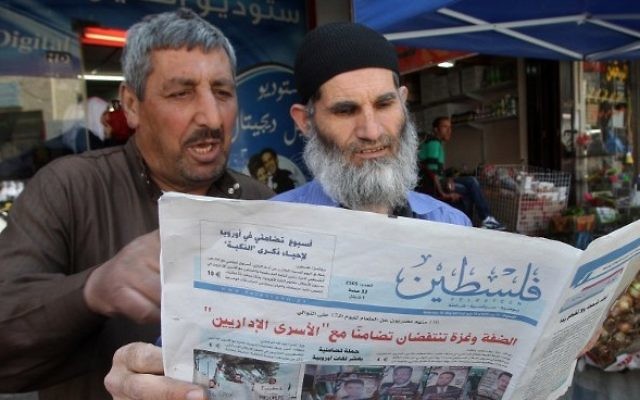 Des Palestiniens qui lisent le journal affilié au Hamas Falastin dans une rue de Hébron (Crédit : Hazem Bader/AFP)