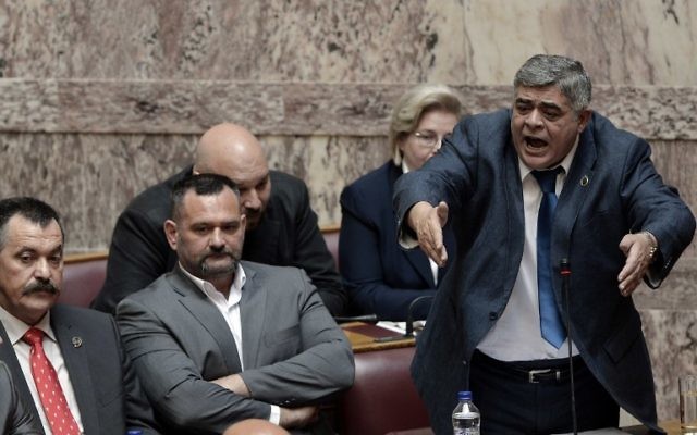 Nikolaos Michaloliakos (debout), le leader du parti néonazi grec Aube dorée pendant son procès, en 2014. (Crédit : AFP/Louisa Gouliamaki)