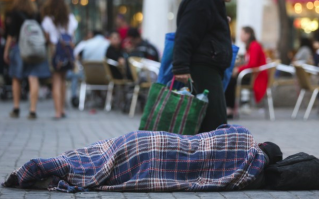 Des gens passent à côté d'un sans-abri qui dort dans la rue, près des cafés du centre de Jérusalem. Le 10 novembre 2013. (Nati Shohat/FLASH90)