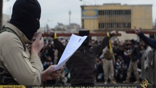 Un combattant de l'Etat islamique lisant les charges contre deux personnes crucifiées (en arrière plan) (Crédit : Capture d'écran) 