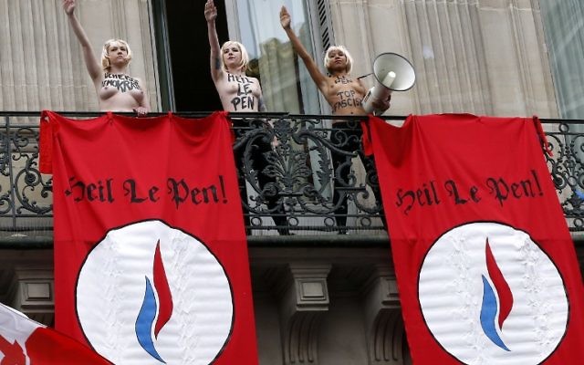 Des activistes Femen effectuant le salut nazi près de drapeaux où  on peut lire "Heil Le Pen", sur un balcon  lors d'un rassemblement FN en l'honneur de Jeanne d'Arc  juste en dessous du balcon où elles se trouvent à Paris le 1er mai 2015 (Crédit : AFP PHOTO / THOMAS SAMSON)
