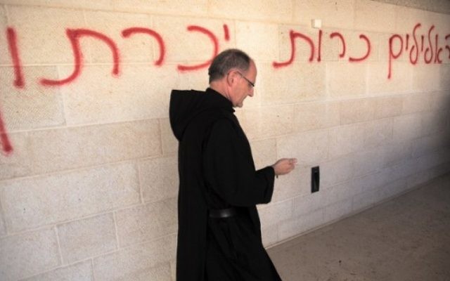 Un prêtre passe à côté d’un graffiti en hébreu, disant « les fausses idoles seront éliminées », pendant qu’il inspecte les dommages à l’église de la Multiplication de Tabgha, sur les rives du lac de Tibériade dans le nord d’Israël, le 18 juin 2015. (Crédits : AFP / Menahem Kahana)