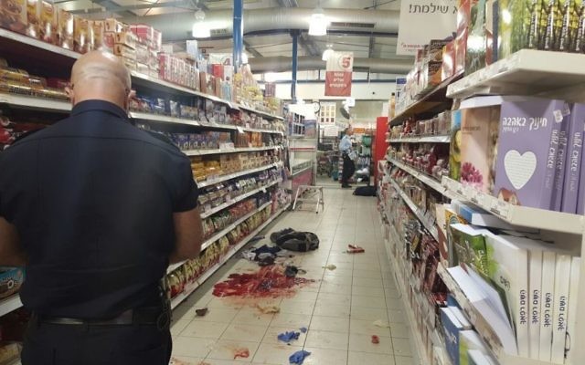 Un policier israélien rassemble des preuves sur les lieux d'une attaque au couteau dans un supermarché dans le parc industriel de Shaar Binyamin, au nord de Jérusalem, le 18 février 2016 (Crédit : Police israélienne)