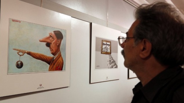 Un Iranien observe une caricature montrant Hitler, lors de la deuxième exposition internationale de dessins et caricatures sur l'Holocauste, à Téhéran, le 14 mai 2016. (Crédit : AFP/Atta Kenare)