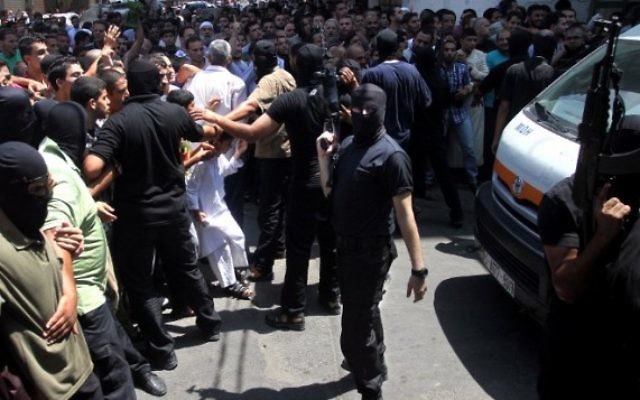 Un Palestinien armé et masqué repousse une foule de croyants devant la mosquée de Gaza Ville après la prière du vendredi, avant l'exécution de 18 hommes qui auraient collaboré avec Israël, le 22 août 2O14. (Crédit : AFP)