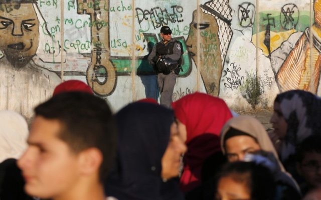 Un policier israélien surveille le checkpoint de Qualandia alors que des Palestiniens le franchissent , 17 juin 2016 (Crédit : AFP /ABBAS MOMANI)