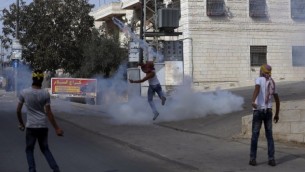 Un jeune Palestinien masqué renvoie des gaz lacrymogènes sur les garde-frontières israéliens pendant des affrontements dans le village palestinien d'al-Ram, entre Jérusalem et Ramallah, en Cisjordanie, le 22 octobre 2015. (Crédit : AFP/Abbas Momani)