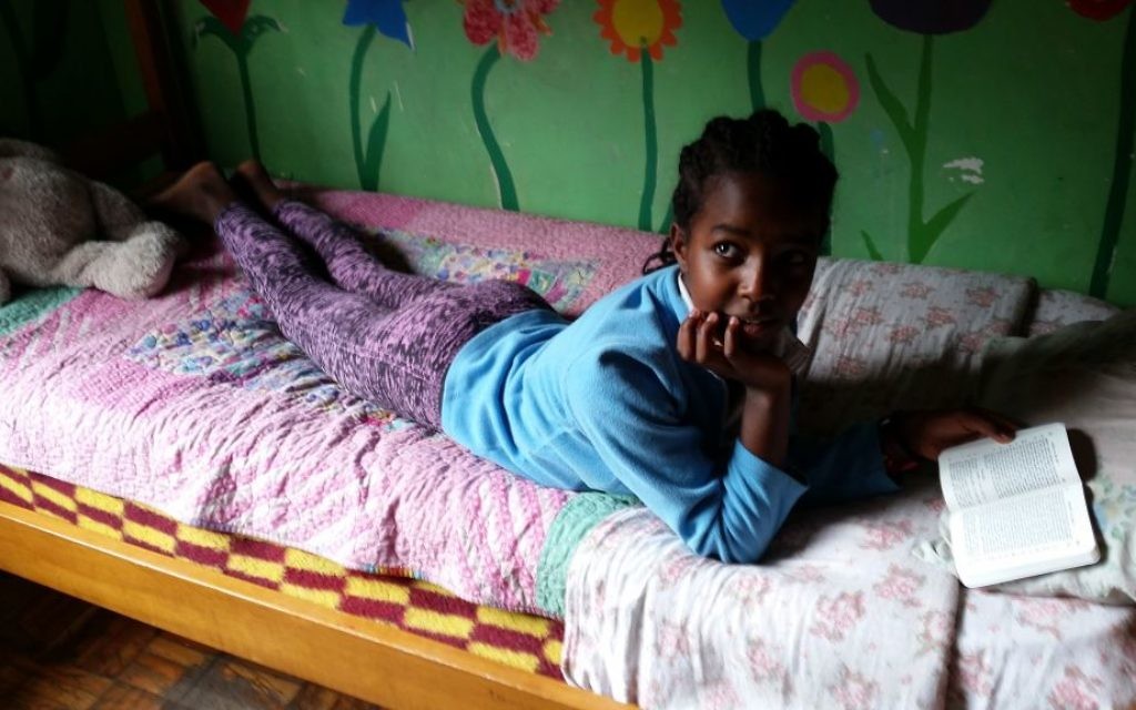 Une fille lit la Bible dans son lit au Centre d'Addis-Abeba AHOPE pour les orphelins séropositifs, le 7 juillet 2016 (Crédit : Raphael Ahren / Times of Israel)