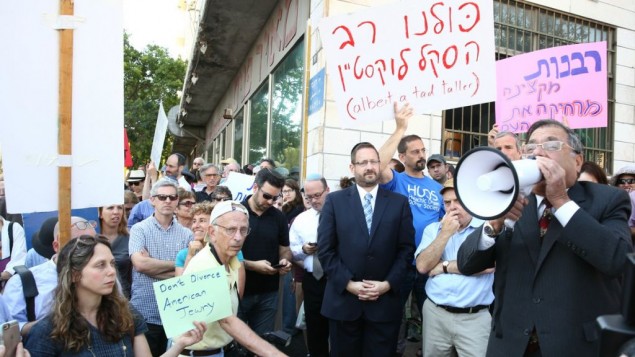 Le grand rabbin d'Efrat Shlomo Riskin parle dans un mégaphone, le 6 juillet 2016, lors d'une manifestation devant les bureaux du grand rabbin de Jérusalem, en soutien aux conversions du rabbin new-yorkais Haskel Lookstein, sous l’œil attentif du chef de l'Agence juive Natan Sharansky et de l'ancien député Dov Lipman (Crédit : Ezra Landau)