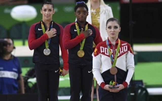 La Russe Aliya Mustafina (à droite), et les Américaines Simone Biles (au centre) et Alexandra Raisman (à gauche), sur le podium de la finale du concours général de gymnastique artistique féminine individuelle au cours des JO de Rio 2016 le 11 août 2016 (AFP Photo/Ben Stansall)