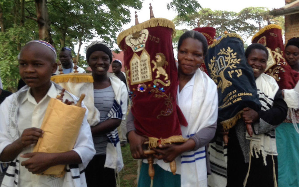 Anticipant la construction d'une nouvelle synagogue à Nabagoye, en Ouganda, les femmes et les enfants ont l'honneur de transférer les rouleaux de la Torah, de la vieille synagogue à une maison temporaire. (Autorisation de Be'chol Lashon, via JTA)